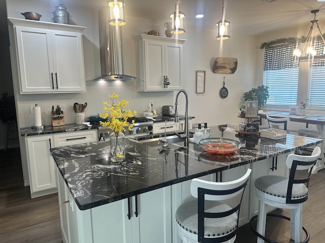 kitchen with wall chimney exhaust hood, decorative light fixtures, and a center island with sink