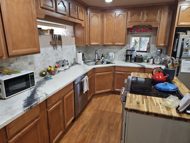 kitchen with brown cabinets, wooden counters, appliances with stainless steel finishes, a sink, and light wood-type flooring