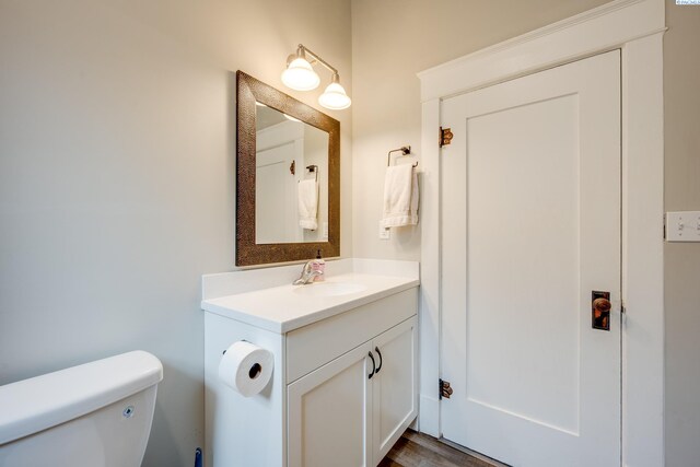 half bathroom with toilet, vanity, and wood finished floors