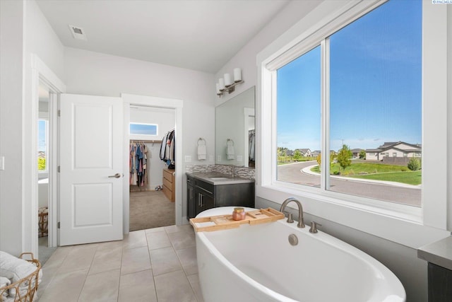 full bathroom featuring a freestanding tub, a walk in closet, vanity, and tile patterned floors