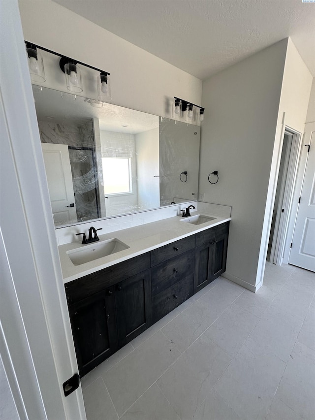 full bathroom with a sink, a tile shower, a textured ceiling, and double vanity