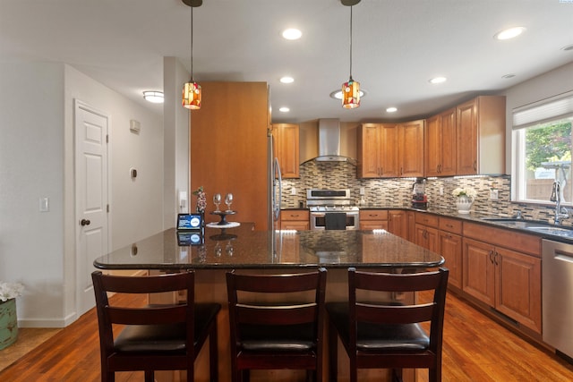 kitchen with wall chimney range hood, appliances with stainless steel finishes, a sink, tasteful backsplash, and dark wood-style floors