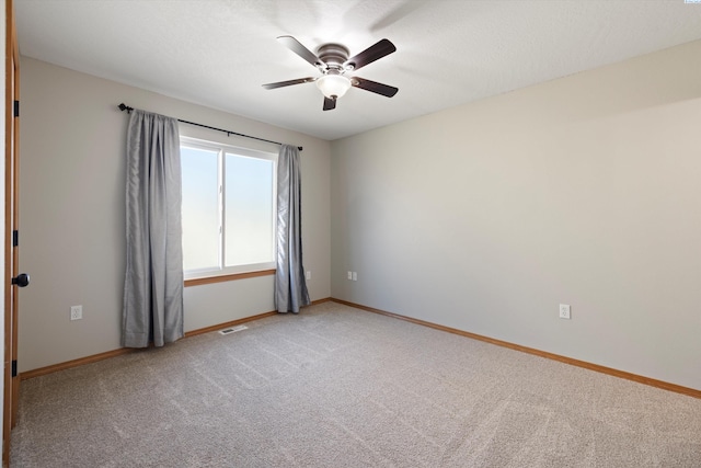 spare room with light colored carpet, visible vents, ceiling fan, and baseboards