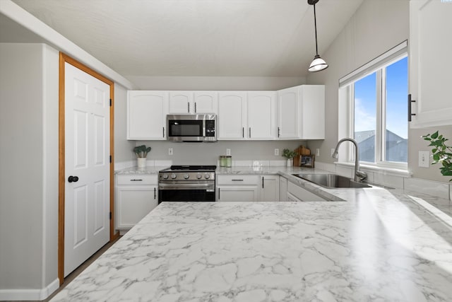 kitchen featuring light stone counters, decorative light fixtures, stainless steel appliances, white cabinetry, and a sink