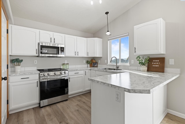 kitchen featuring a peninsula, a sink, white cabinets, vaulted ceiling, and appliances with stainless steel finishes