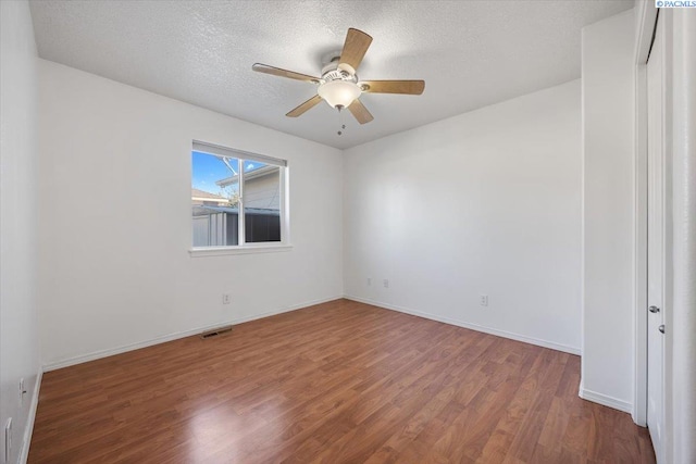 spare room with baseboards, visible vents, a ceiling fan, wood finished floors, and a textured ceiling