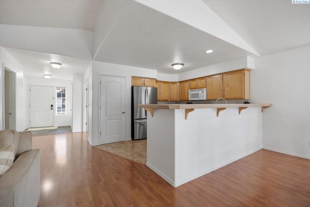 kitchen featuring white microwave, a kitchen breakfast bar, open floor plan, freestanding refrigerator, and a peninsula