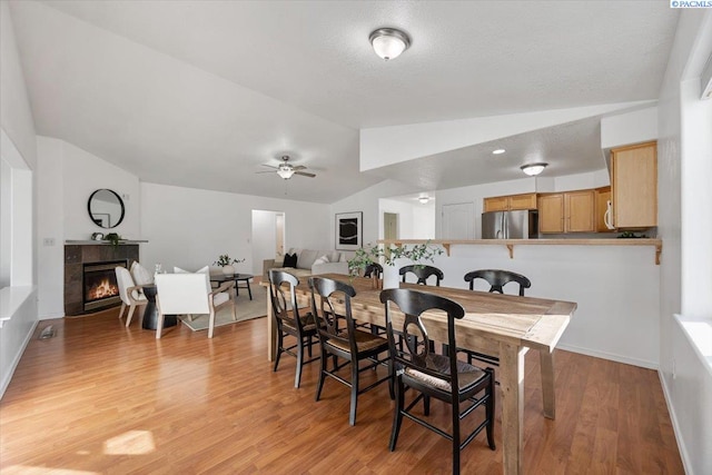 dining space featuring a fireplace, vaulted ceiling, ceiling fan, light wood-type flooring, and baseboards