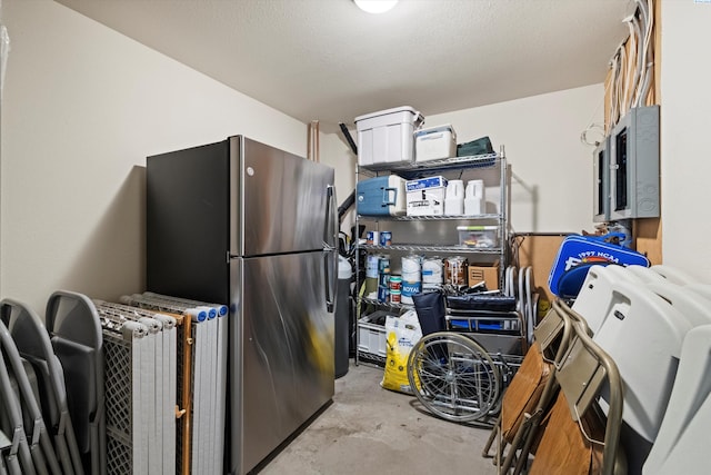 kitchen featuring electric panel, unfinished concrete floors, a textured ceiling, and freestanding refrigerator