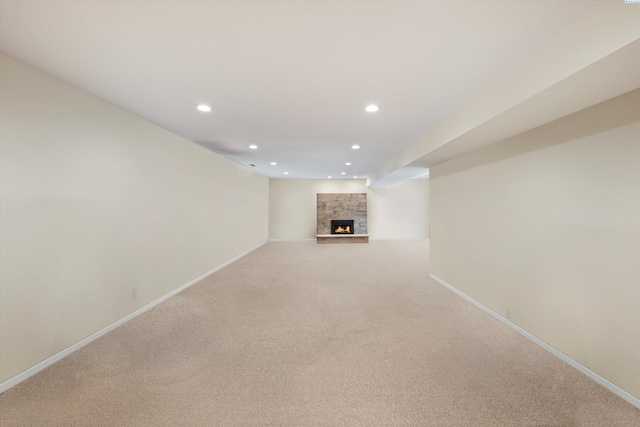 unfurnished living room featuring recessed lighting, light carpet, a stone fireplace, and baseboards