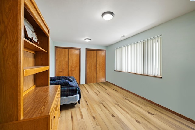 bedroom with visible vents, two closets, and light wood-style flooring