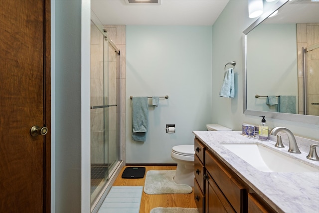 bathroom with toilet, a stall shower, vanity, wood finished floors, and baseboards