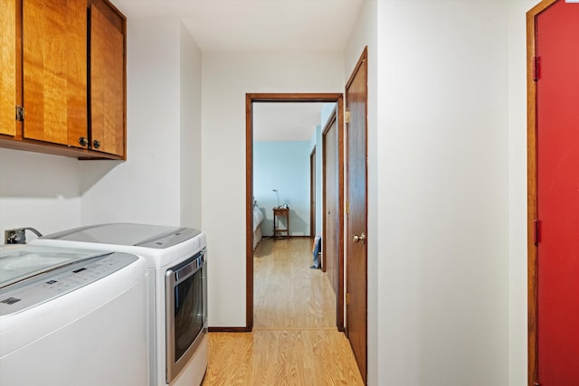 clothes washing area with light wood-type flooring, cabinet space, baseboards, and washer and dryer