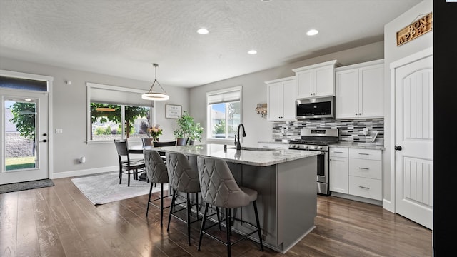 7104 W 31st Pl, Kennewick, WA 99338 - kitchen featuring appliances with stainless steel finishes, dark wood-style flooring, decorative backsplash, a center island with sink, and light stone countertops