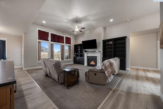 living room with ceiling fan, recessed lighting, baseboards, light wood finished floors, and a glass covered fireplace