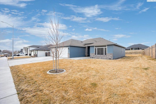 view of front of property with concrete driveway, stone siding, roof with shingles, an attached garage, and a front lawn