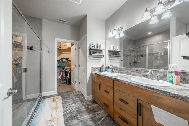 bathroom with a sink, visible vents, a spacious closet, a shower stall, and double vanity