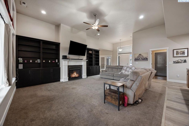 living area with visible vents, baseboards, a glass covered fireplace, a towering ceiling, and ceiling fan