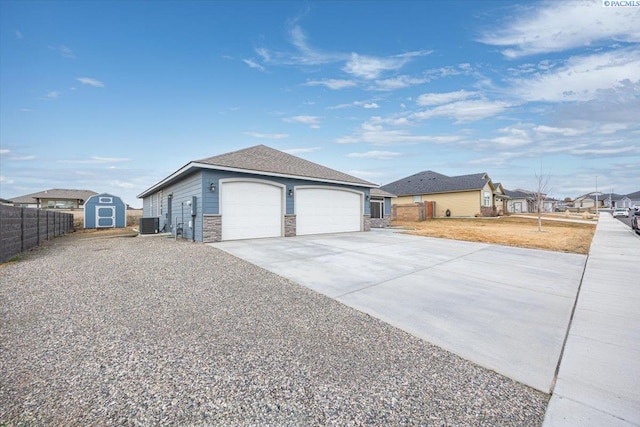 view of side of home featuring an outbuilding, concrete driveway, an attached garage, fence, and stone siding