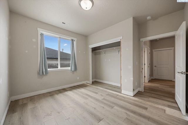 unfurnished bedroom with light wood finished floors, baseboards, visible vents, and a closet