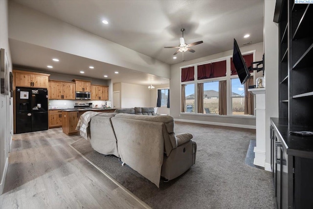 living area with baseboards, lofted ceiling, ceiling fan with notable chandelier, light wood-style floors, and recessed lighting