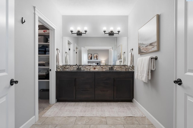 full bath with double vanity, a spacious closet, baseboards, and a sink