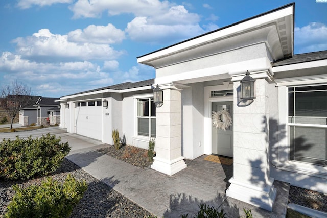 doorway to property featuring an attached garage, driveway, and stucco siding