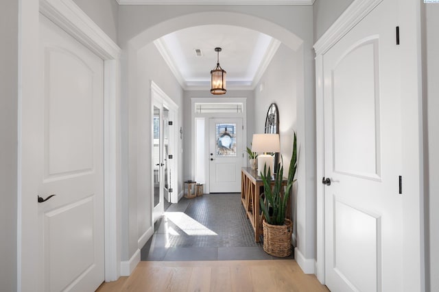 foyer entrance featuring arched walkways, visible vents, ornamental molding, wood finished floors, and baseboards