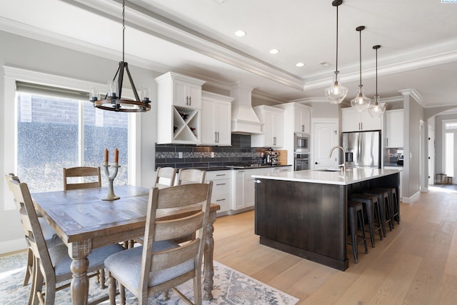 kitchen with a raised ceiling, stainless steel appliances, light wood-type flooring, and custom exhaust hood