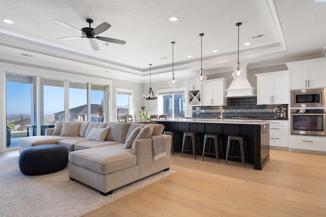 living room featuring light wood-style floors, a tray ceiling, and ornamental molding