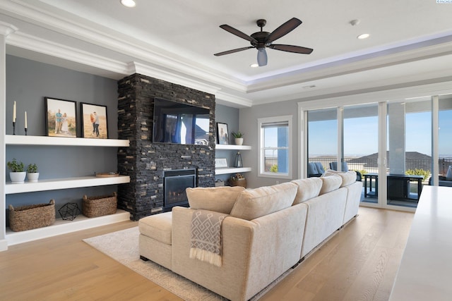 living area with a wealth of natural light, a raised ceiling, a fireplace, and wood finished floors