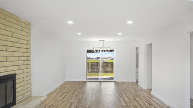 unfurnished living room with light hardwood / wood-style flooring, a notable chandelier, and a fireplace