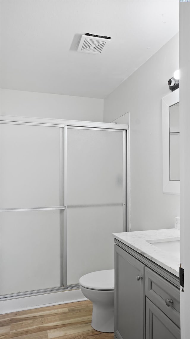 bathroom featuring hardwood / wood-style flooring, vanity, toilet, and a shower with shower door