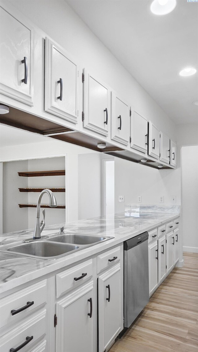 kitchen with sink, white cabinetry, light wood-type flooring, stainless steel dishwasher, and light stone countertops