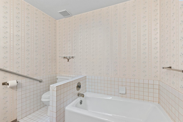 bathroom featuring toilet, tile walls, a textured ceiling, a bathtub, and tile patterned flooring