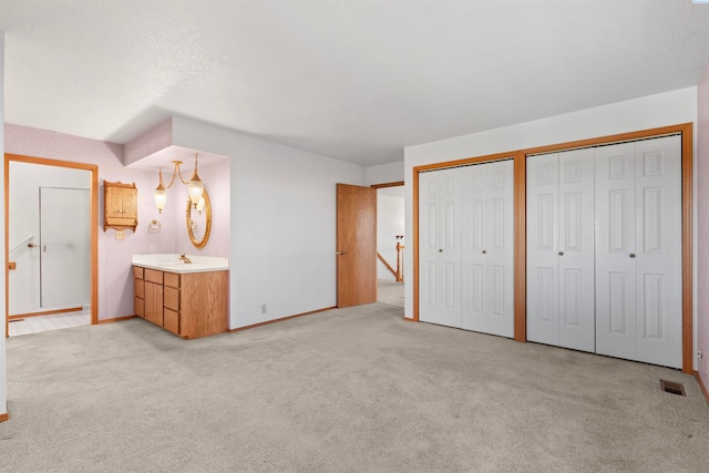 unfurnished bedroom with multiple closets, light colored carpet, ensuite bathroom, and sink