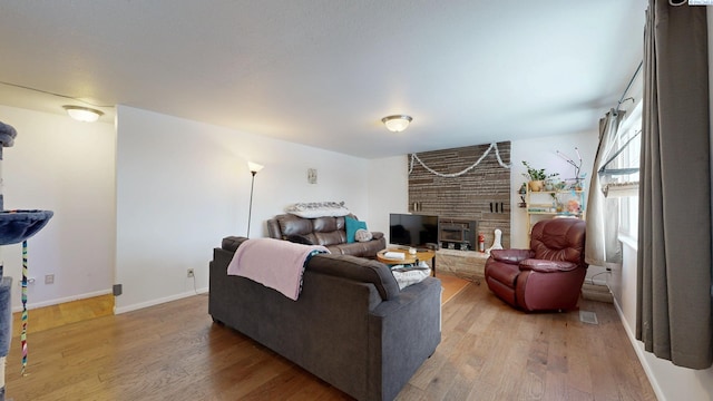 living room featuring a large fireplace, baseboards, and wood finished floors