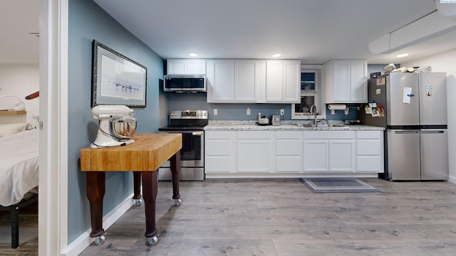 kitchen with appliances with stainless steel finishes, sink, white cabinets, light stone countertops, and light wood-type flooring