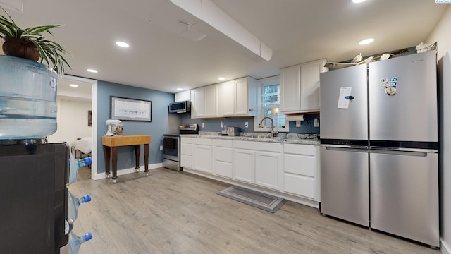 kitchen featuring sink, white cabinetry, light stone counters, light wood-type flooring, and stainless steel appliances