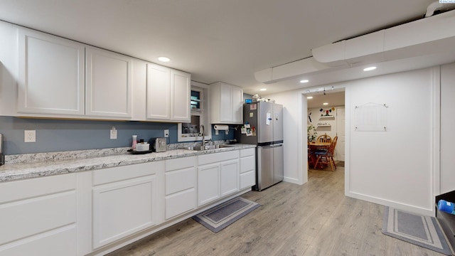 kitchen with sink, white cabinetry, light hardwood / wood-style flooring, stainless steel fridge, and light stone countertops