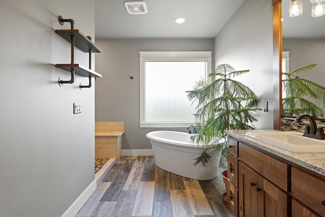 full bath featuring visible vents, vanity, wood finished floors, a freestanding tub, and baseboards