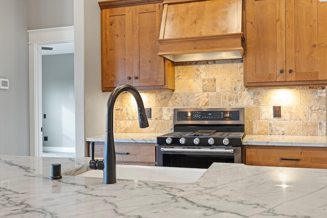 kitchen featuring light stone countertops, tasteful backsplash, stainless steel range with gas cooktop, and extractor fan