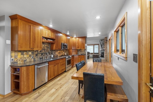 kitchen featuring sink, backsplash, stainless steel appliances, light hardwood / wood-style floors, and dark stone counters