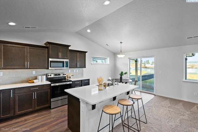 kitchen with lofted ceiling, stainless steel appliances, tasteful backsplash, a center island with sink, and decorative light fixtures