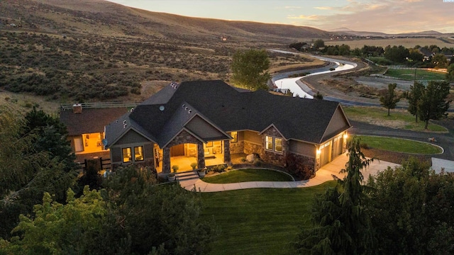 back house at dusk with a garage, a mountain view, and a lawn