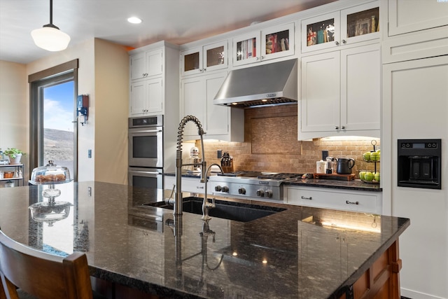 kitchen with tasteful backsplash, decorative light fixtures, double oven, dark stone counters, and white cabinets