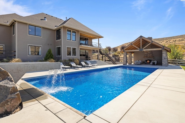 view of pool with pool water feature, a gazebo, an outdoor fireplace, ceiling fan, and a patio