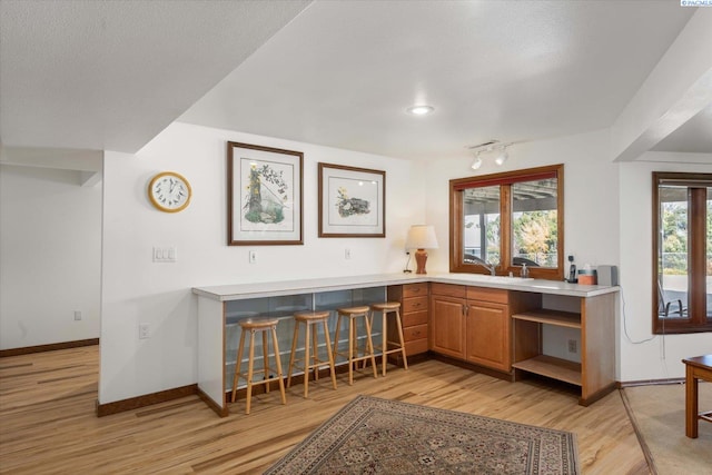 kitchen with light wood-style flooring, a breakfast bar, baseboards, light countertops, and brown cabinets