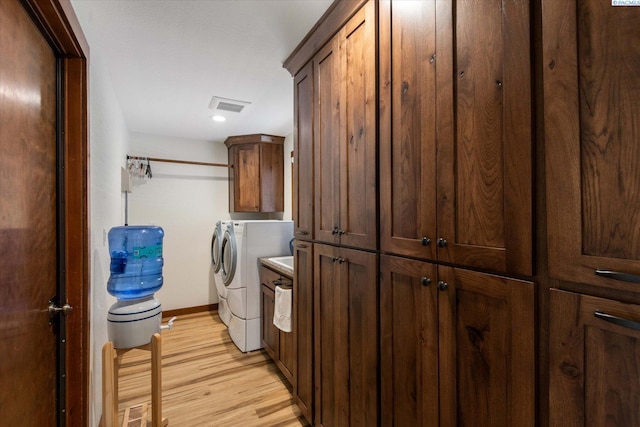 clothes washing area featuring light wood-style flooring, visible vents, baseboards, independent washer and dryer, and cabinet space