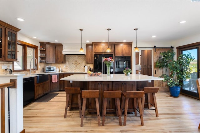 kitchen with a barn door, light wood-style floors, light countertops, black appliances, and open shelves